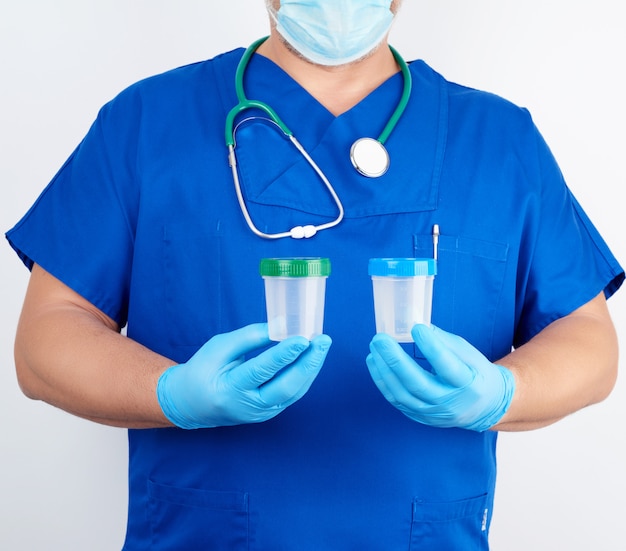 Doctor en uniforme azul y guantes de látex sostiene un recipiente de plástico vacío para tomar muestras de orina.