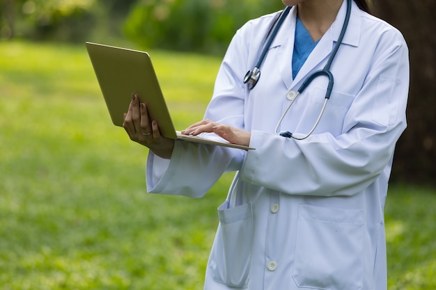 Doctor en uniforme blanco con estetoscopio y portátil jardín del hospital