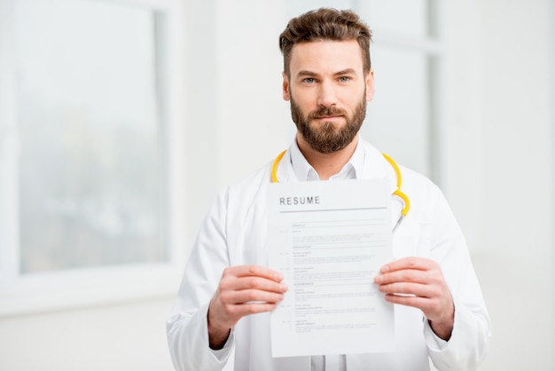 Doctor en uniforme con currículum vitae para contratación laboral en el interior blanco