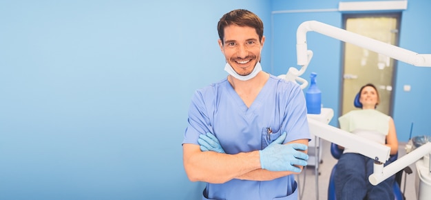 Doctor en uniforme médico azul en consultorio de odontología y paciente en el sillón dental