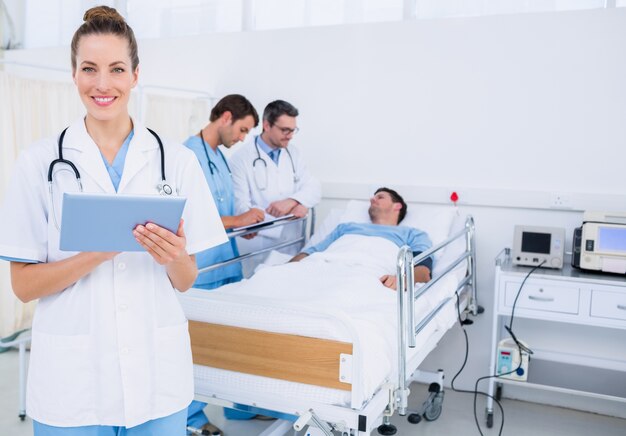Doctor usando tableta digital con colegas y paciente detrás