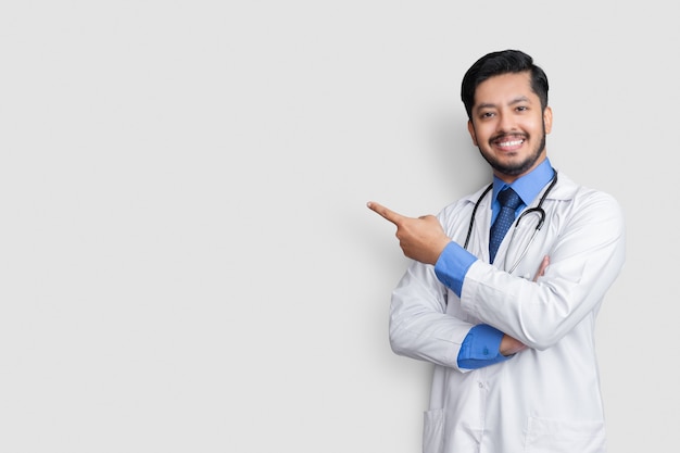 Doctor vistiendo uniforme sonriendo mientras presenta y apunta aislado en la pared azul con espacio de copia