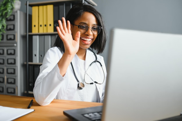 Una doctora africana habla con un paciente para realizar telemedicina en línea, videollamada con cámara web Mujer terapeuta videoconferencia en computadora en telemedicina remota portátil chat virtual Concepto de telesalud