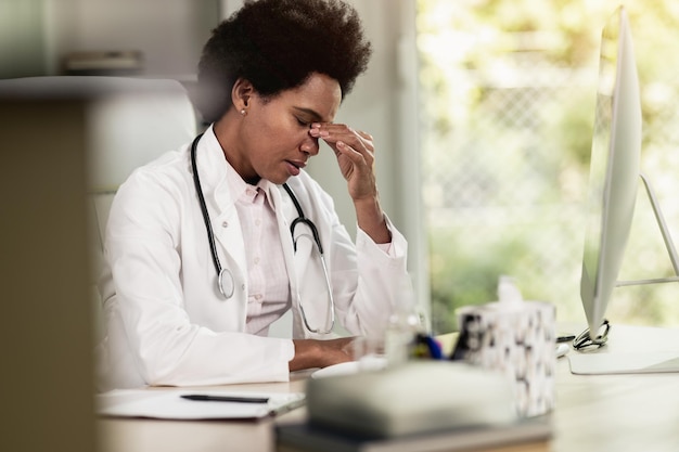 Una doctora afroamericana cansada sentada sola en su consultorio.