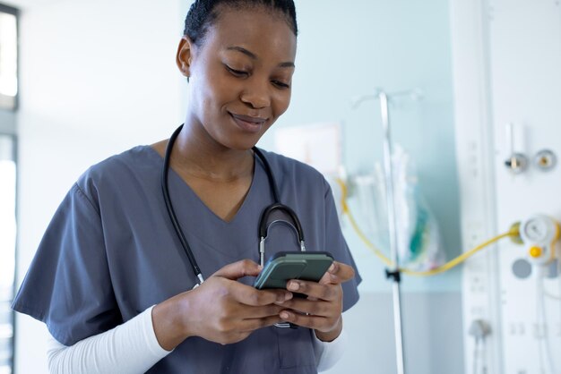 Doctora afroamericana feliz usando un teléfono inteligente en la habitación del hospital