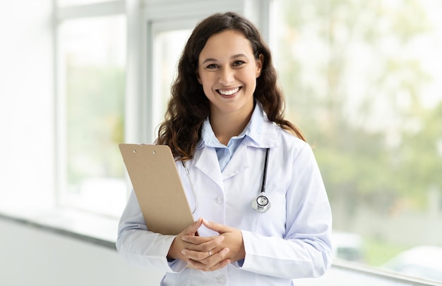 Foto doctora alegre en bata blanca con estetoscopio y clipboard