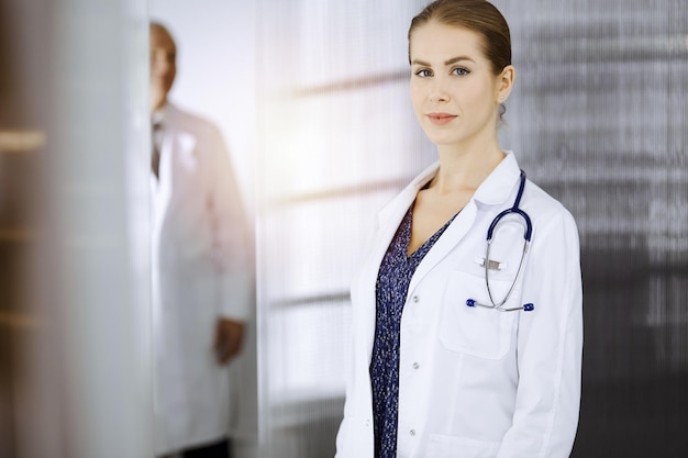 Una doctora alegre parada en una clínica soleada. Retrato de mujer-médico sonriente amistosa. Concepto de medicina.