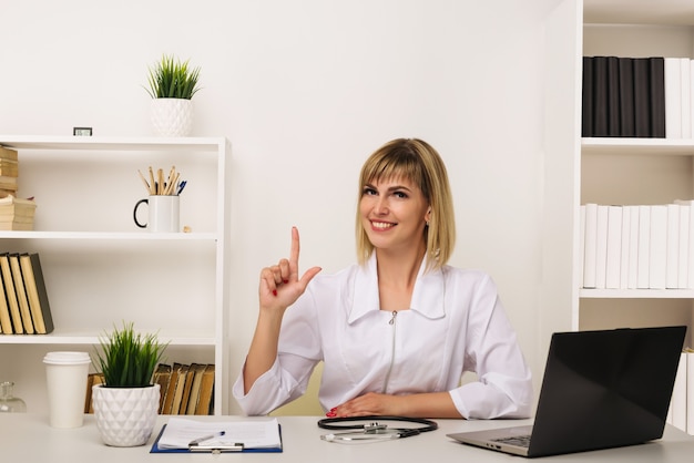 Doctora amable trabaja en su escritorio en la oficina apuntando hacia arriba