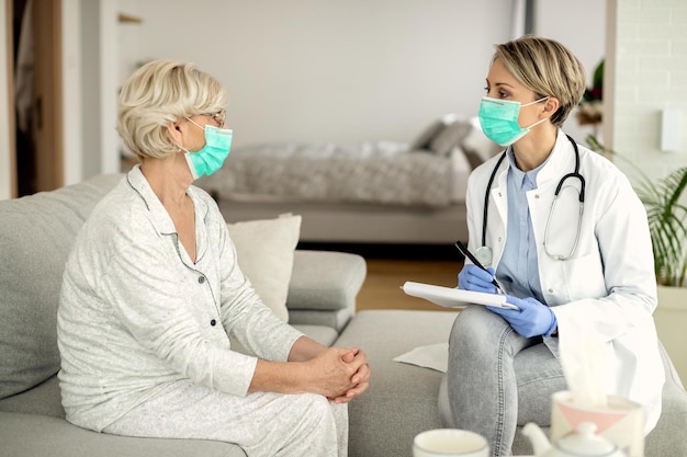 Doctora y anciana con mascarillas durante una visita a casa