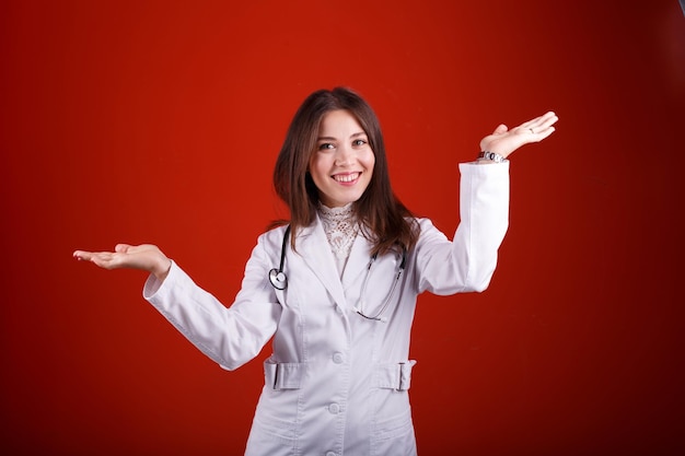 Foto doctora apuntando a algo sobre un fondo rojo.