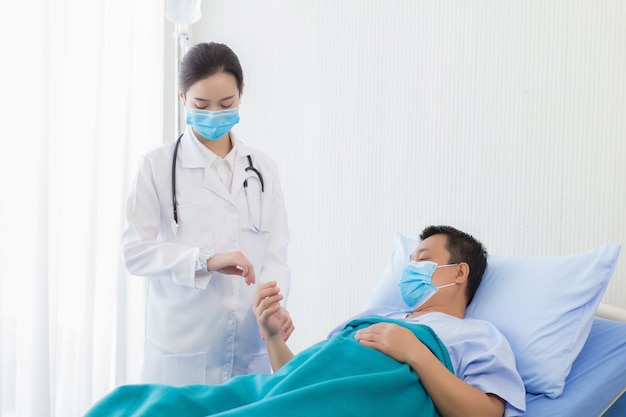 La doctora asiática está tomando el pulso en la muñeca de un paciente hombre para controlar la frecuencia cardíaca.