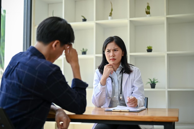 Una doctora asiática estresada y seria está teniendo una reunión seria con un paciente