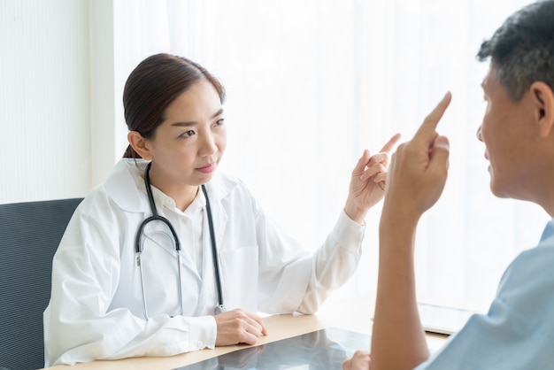 Doctora asiática y paciente discutiendo algo mientras está sentado en la mesa