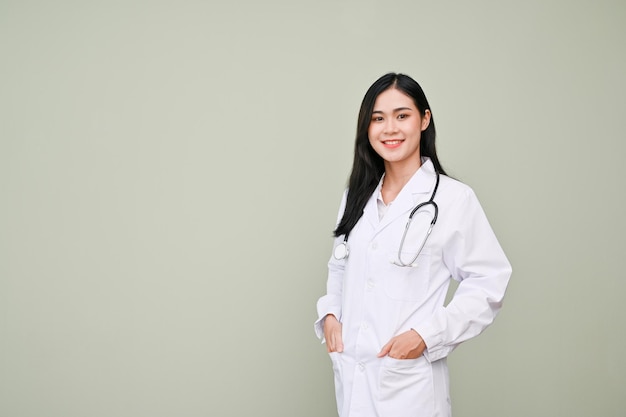 Doctora asiática profesional en uniforme de pie contra el fondo gris