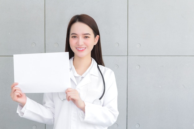 Doctora asiática que usa bata médica sostiene y muestra papel blanco para presentar algo