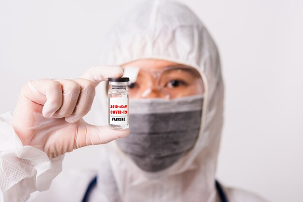 Doctora asiática en uniforme de PPE y guantes con mascarilla protectora en laboratorio sosteniendo frasco de medicina botella de vacuna de coronavirus