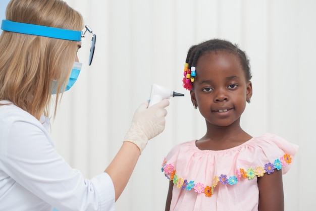 Doctora auscultando el oído del pequeño niño africano.