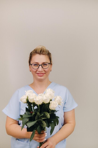 Una doctora en bata azul con un ramo de rosas blancas en las manos