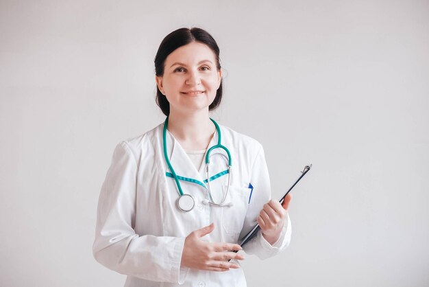 Doctora en una bata blanca con una carpeta en las manos y un estetoscopio sobre un fondo blanco.