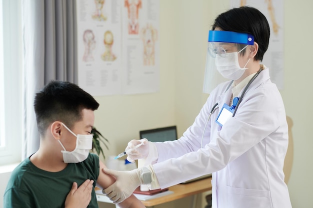 Doctora con bata blanca y máscara protectora inyectando a un niño pequeño durante su visita al hospital