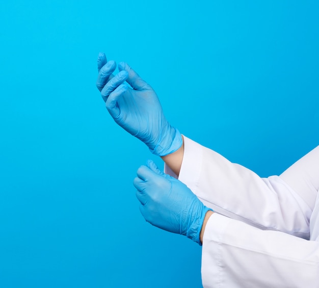 Foto doctora en una bata blanca pone en sus manos guantes médicos estériles de látex azul en sus manos