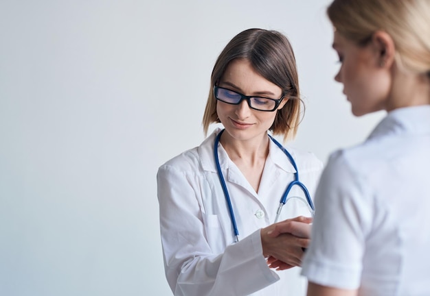 Doctora con bata médica y anteojos con un estetoscopio alrededor del cuello y una paciente