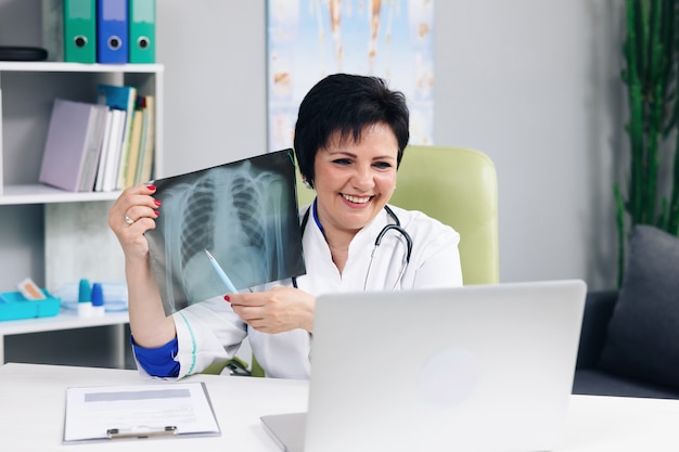 Doctora en bata médica blanca haciendo una llamada de conferencia en una computadora portátil que consulta a un paciente a distancia en línea en un chat de video, explica el tratamiento mediante el concepto de cámara web