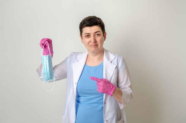 Doctora en bata médica sostiene una máscara única en la mano, señalando con disgusto con el dedo.