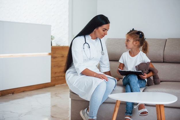 Doctora con Bloc de notas se sienta en la clínica con niña.