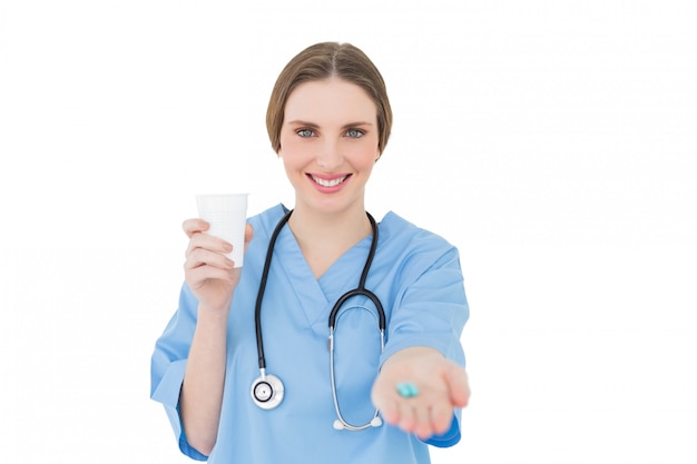 Doctora bonita sosteniendo una taza de plástico y dando píldoras azules