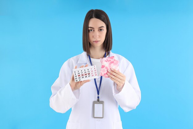 Doctora con calendario de período y almohadillas sobre fondo azul.