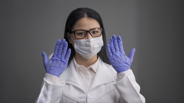 Doctora cansada con uniforme blanco levantó las manos en guantes desechables.