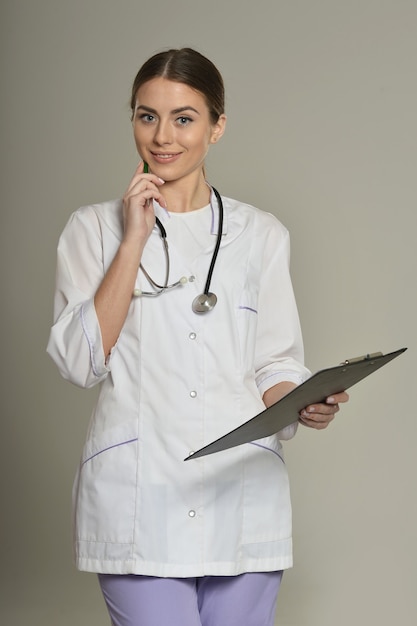 Doctora con una carpeta, de pie sobre fondo gris