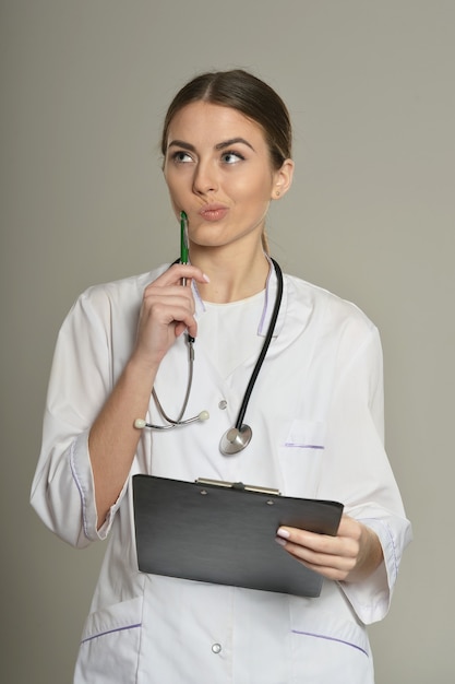 Doctora con una carpeta, de pie sobre fondo gris