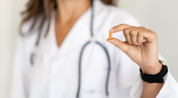 Una doctora caucásica madura con bata blanca muestra un suplemento alimenticio de vitaminas en cápsulas en la clínica
