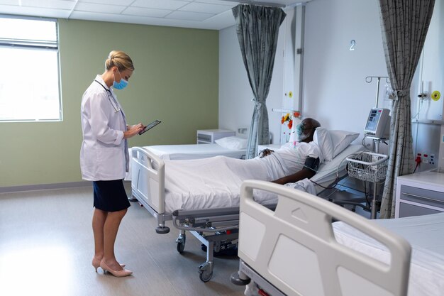 Foto doctora caucásica con mascarilla comprobando la documentación de un paciente masculino en una tableta