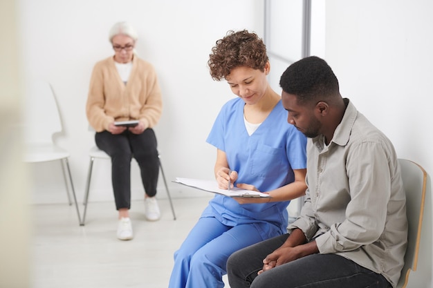 Doctora caucásica sentada en una silla en el pasillo del hospital mostrando los resultados de los análisis de sangre a su paciente afroamericano