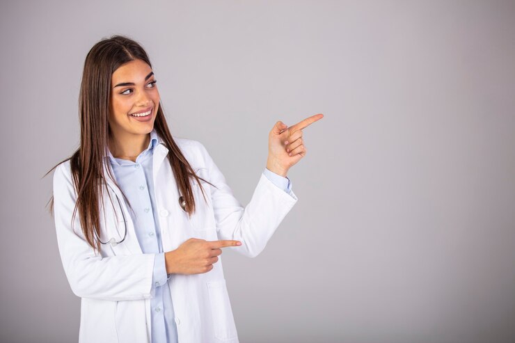 Doctora confía en uniforme blanco mirando a otro lado y apuntando mientras está de pie contra el fondo gris. ¡Mira allá! Esto es lo que recomienda su médico.