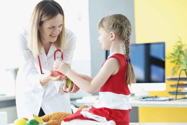 Foto doctora dando manzana de niño pequeño en la clínica