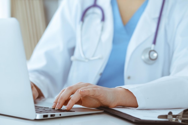 Una doctora desconocida escribiendo en una computadora portátil mientras está sentada en la mesa. Concepto de medicina.