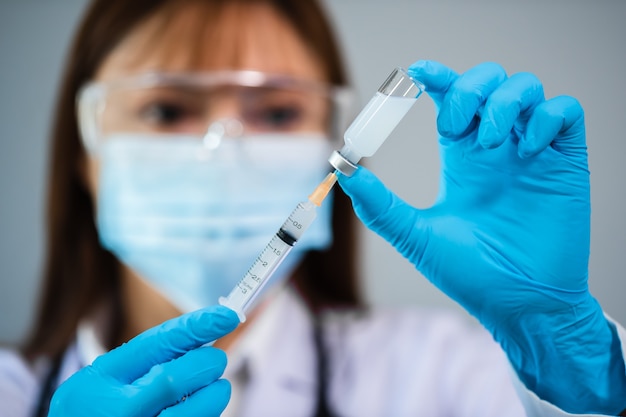 Doctora dibujando la botella de la vacuna en la jeringa de medicina de inyección