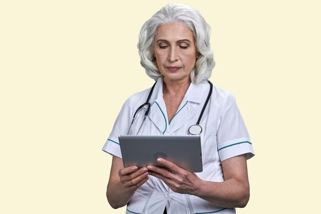 Doctora envejecida seria usando tablet pc fondo amarillo pálido
