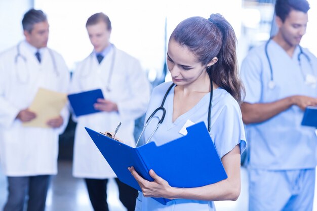 Foto doctora escribiendo un informe médico y colegas parados detrás