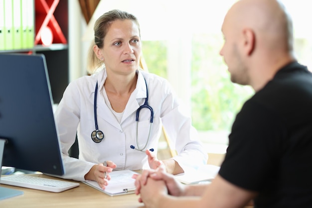 La doctora escucha atentamente la historia de los pacientes sobre su enfermedad sentada en la mesa del hospital