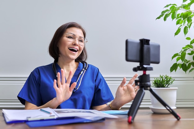 Doctora con un estetoscopio consultando en línea usando un teléfono inteligente en un trípode