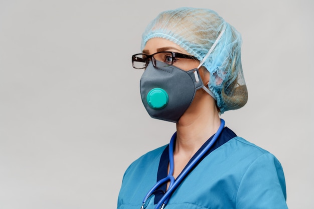 Doctora con estetoscopio con máscara protectora y guantes de látex sobre pared gris claro