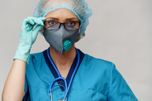 Doctora con estetoscopio con máscara protectora y guantes de látex sobre pared gris claro