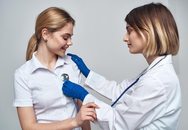 Una doctora con un estetoscopio sostiene a un paciente por el hombro sobre un fondo claro