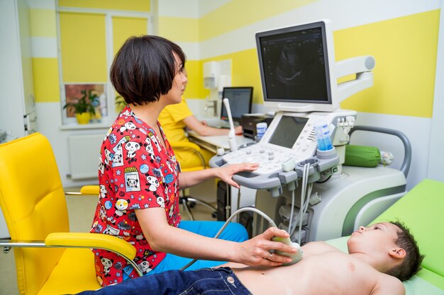 Doctora examinando al niño con equipo ultrasónico en el hospital