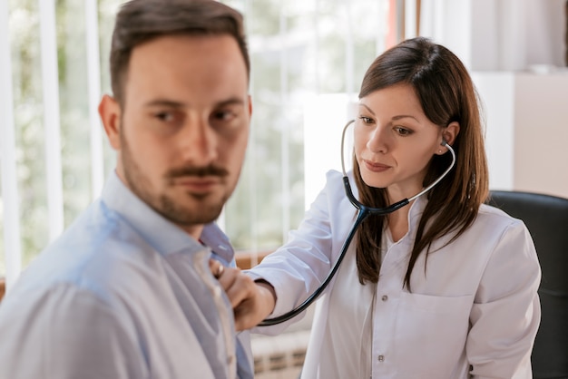 Foto doctora examinando al paciente con su estetoscopio en el hospital